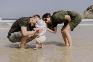 Dad holding baby in the sea - with her toes in the water -- Mum looking on