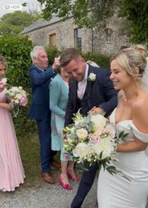 bride and groom smiling as they walk through a confetti aisle